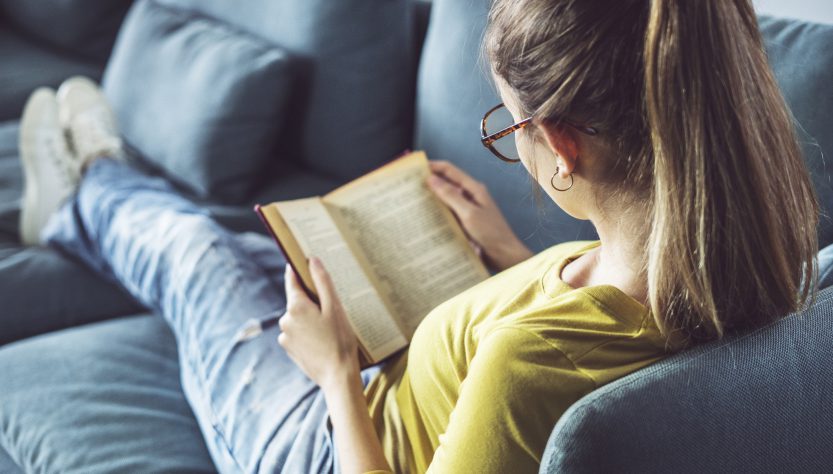 Kvinna sitter i en soffa och läser en bok